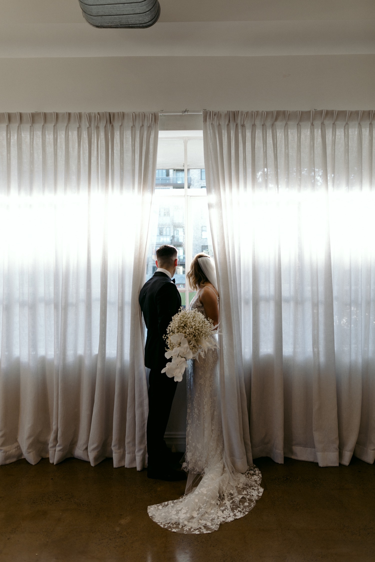 bride and groom looking out of la porte space window at guests below