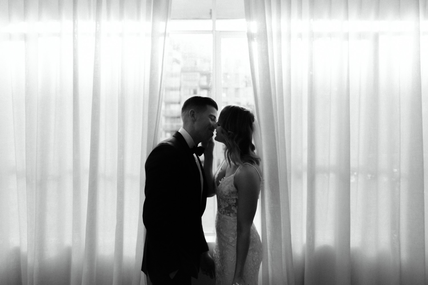 bride and groom kissing in front of window